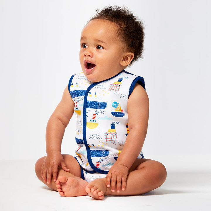 Little one wearing a neoprene baby wrap wetsuit in white with navy trims and boats themed print. Side.