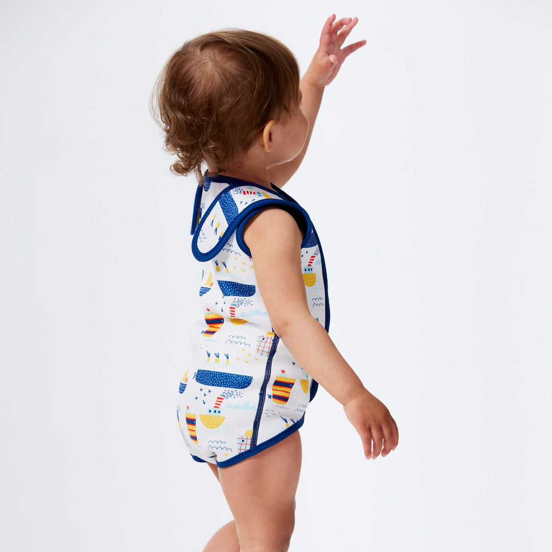 Little one wearing a neoprene baby wrap wetsuit in white with navy trims and boats themed print. Back.