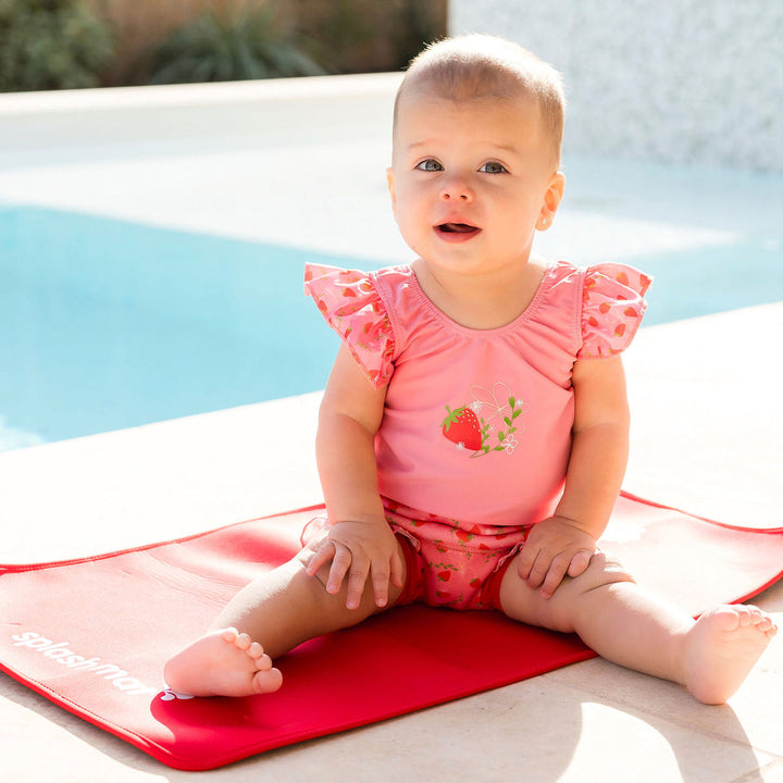 Little one wearing Happy Nappy Costume in pink with red trims and strawberries themed print, featuring frills in arms and leg.