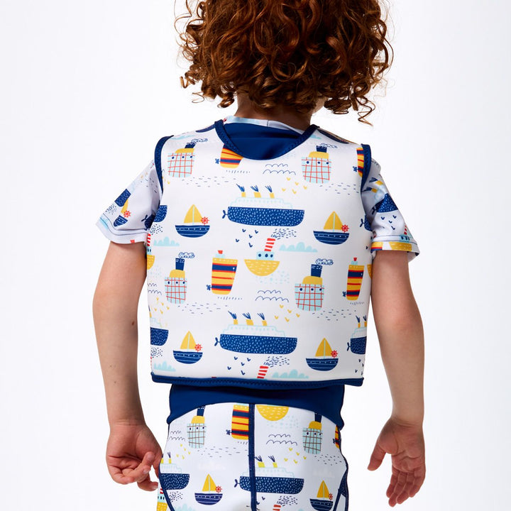 Lifestyle image of child wearing neoprene swim vest for toddlers with non-removable floats in white, navy trims and boats themed print. He's also wearing matching Happy Nappy. Back.