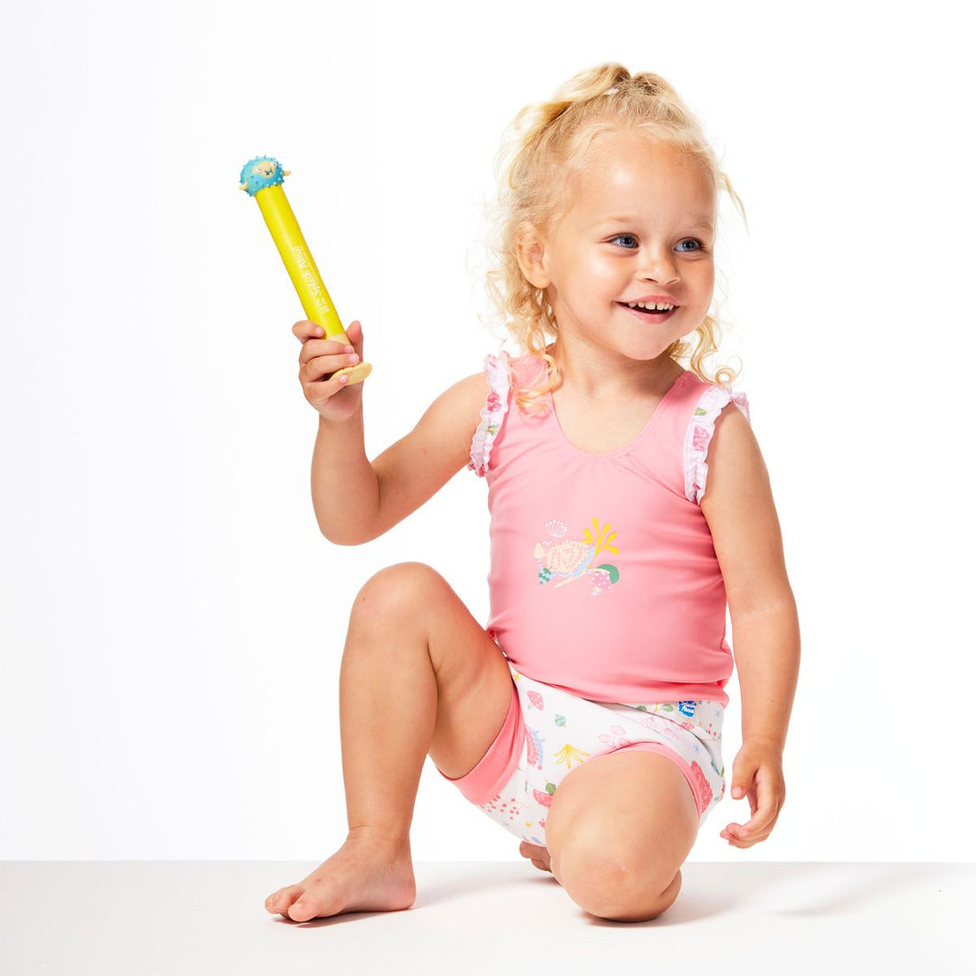 Lifestyle image of child wearing a Happy Nappy Costume in pink and white featuring forest themed print, including hedgehogs, mushrooms and leaves. Front.