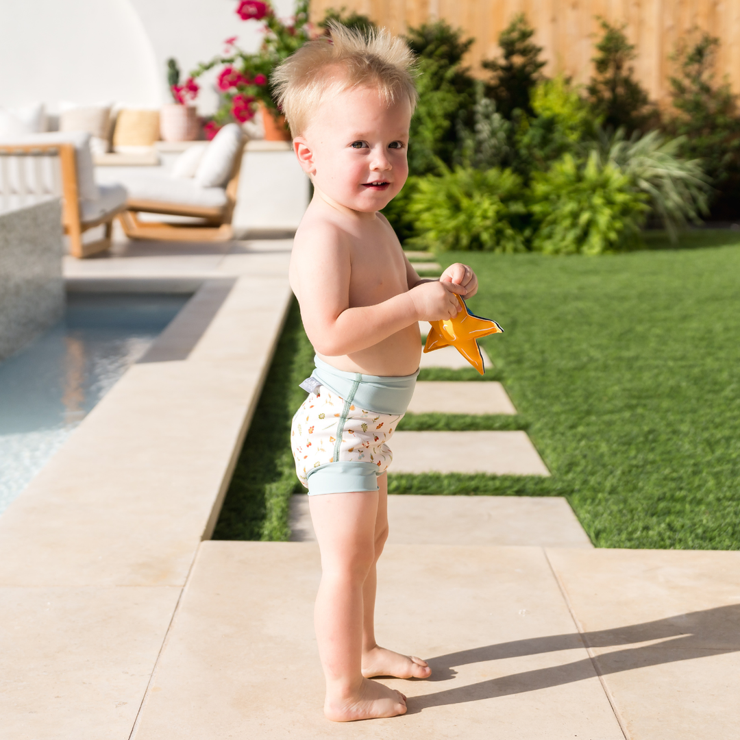 Child wearing reusable swim nappy in white with light blue ribs and Autumn themed print. Side