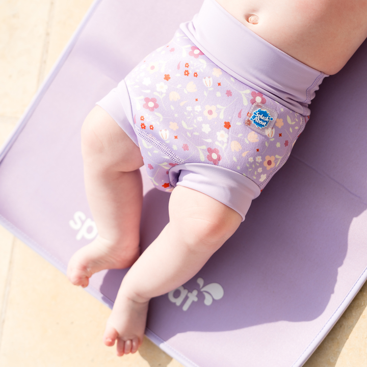 Child wearing reusable swim nappy in lilac and floral themed print. Front.