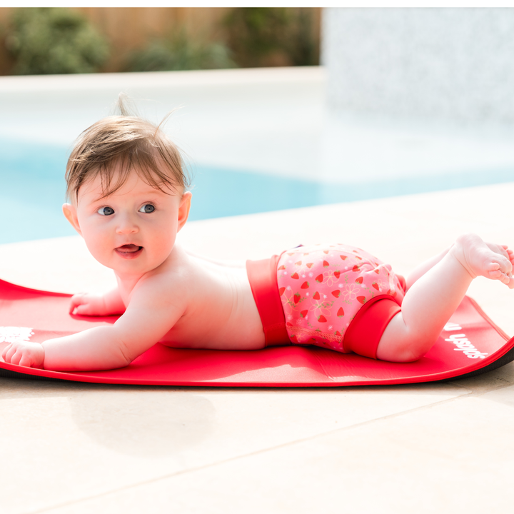 Baby wearing reusable swim nappy in pink with red ribs and strawberries themed print. Side