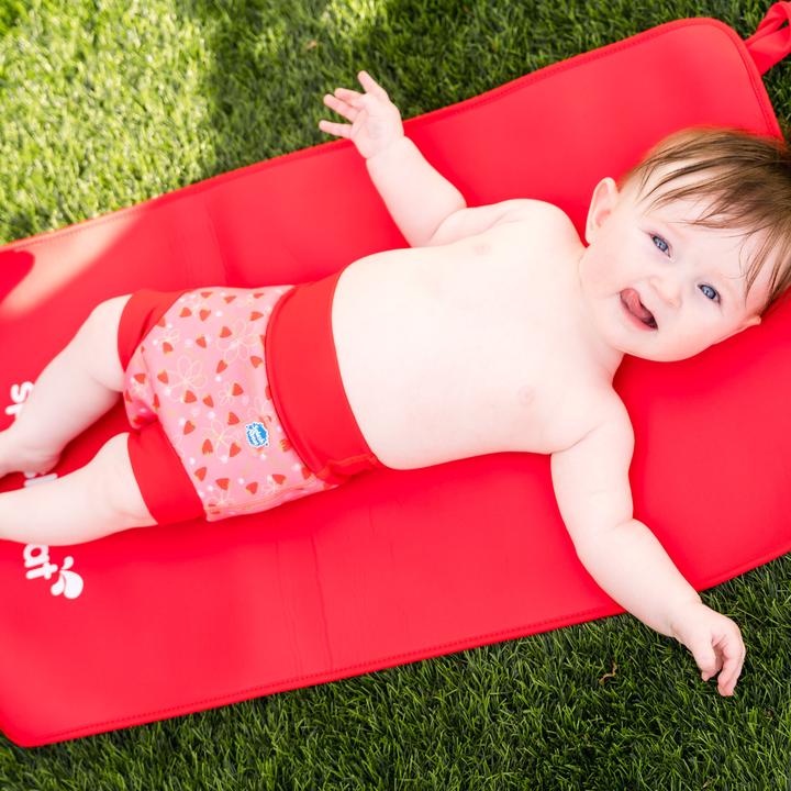 Baby wearing reusable swim nappy in pink with red ribs and strawberries themed print. Front