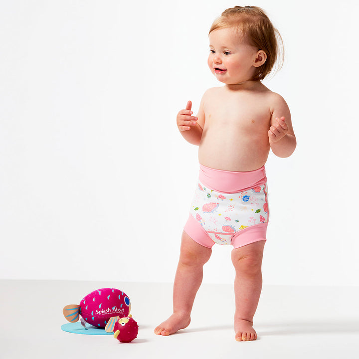 Little one wearing Happy Nappy in white featuring forest themed print. Light pink trims. Front.