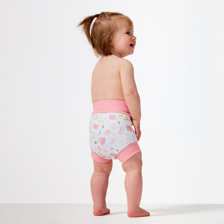 Little one wearing Happy Nappy in white featuring forest themed print. Light pink trims. Back.