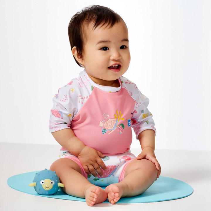 Lifestyle image of child wearing Happy Nappy Sunsuit in pink and forest themed print, including hedgehogs, mushrooms and leaves. Side.