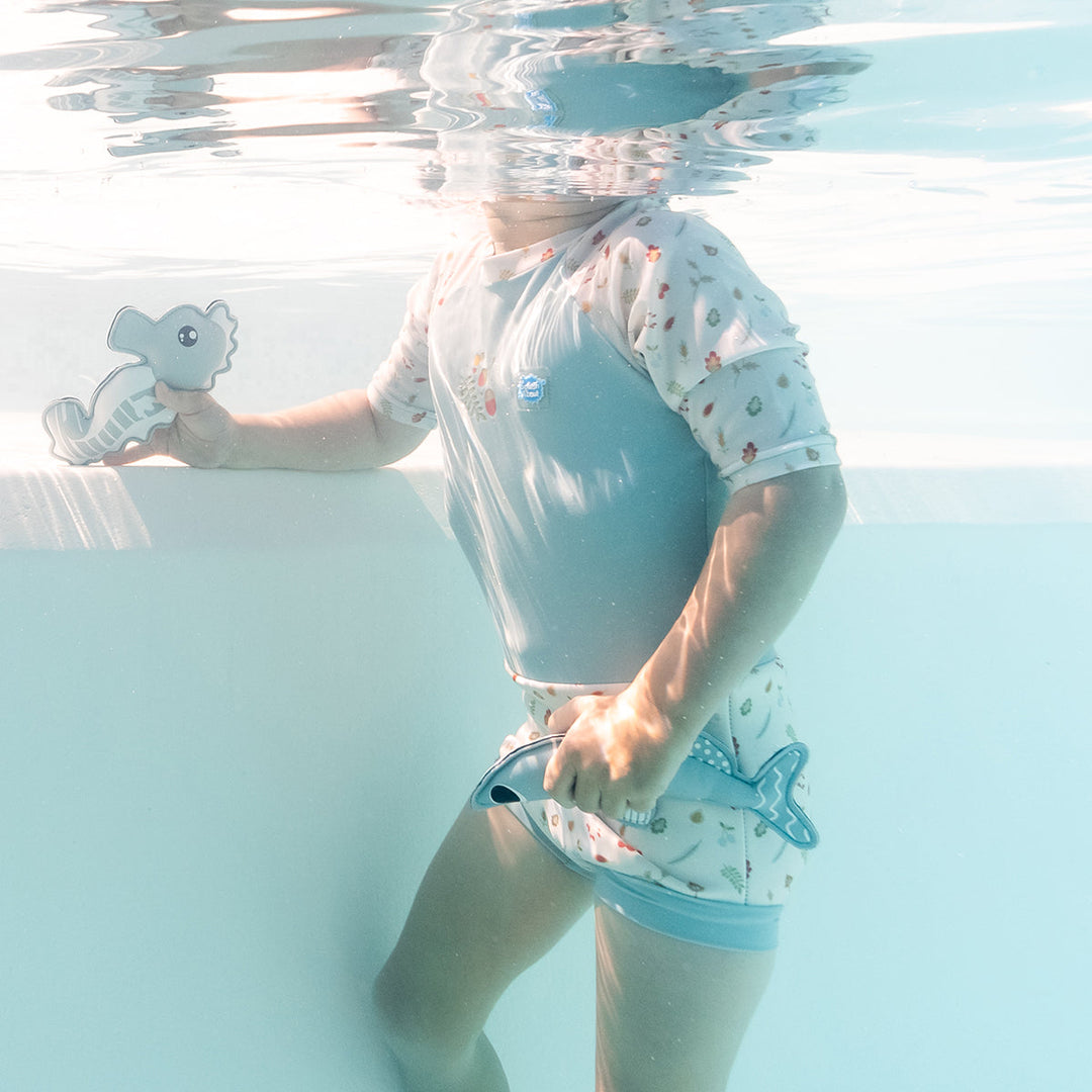 Close up image of child in the pool, wearing Happy Nappy Sunsuit in light blue and white, and acorns and leaves themed print.