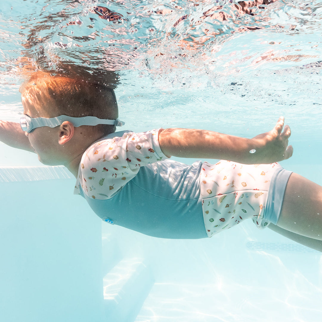 Child swimming in Happy Nappy Sunsuit in light blue and white, and acorns and leaves themed print.