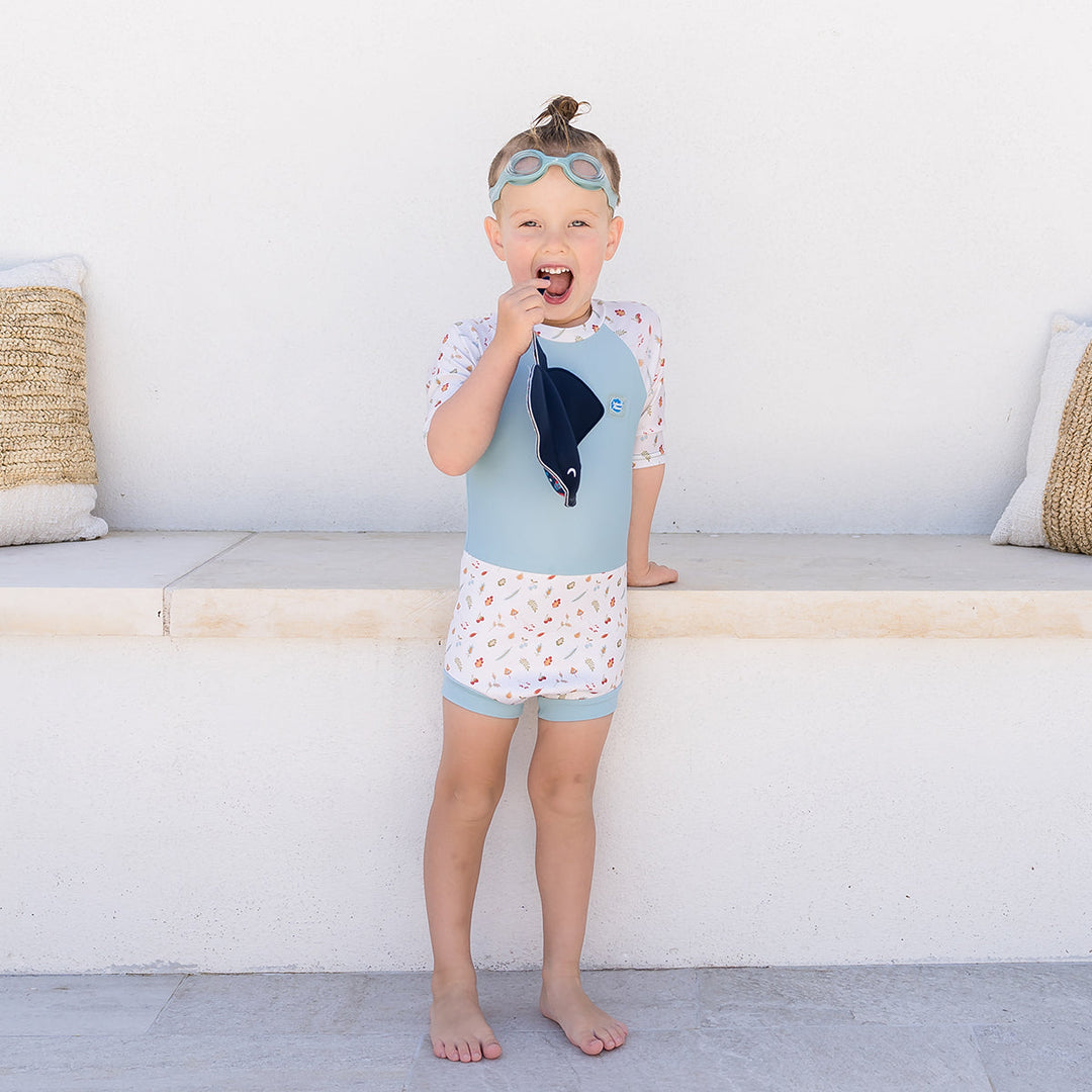 Child wearing Happy Nappy Sunsuit in light blue and white, and acorns and leaves themed print. Front.