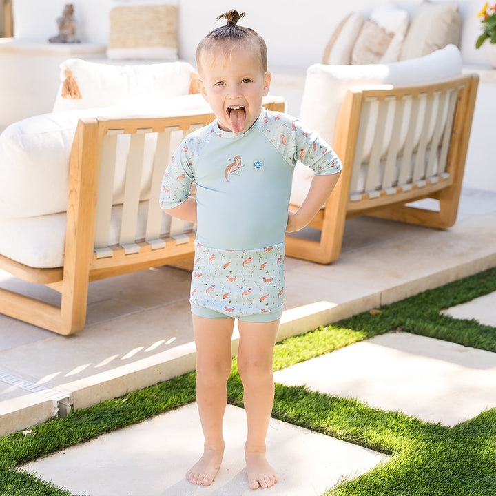 Child wearing Happy Nappy Sunsuit in light blue and otters themed print. Front.