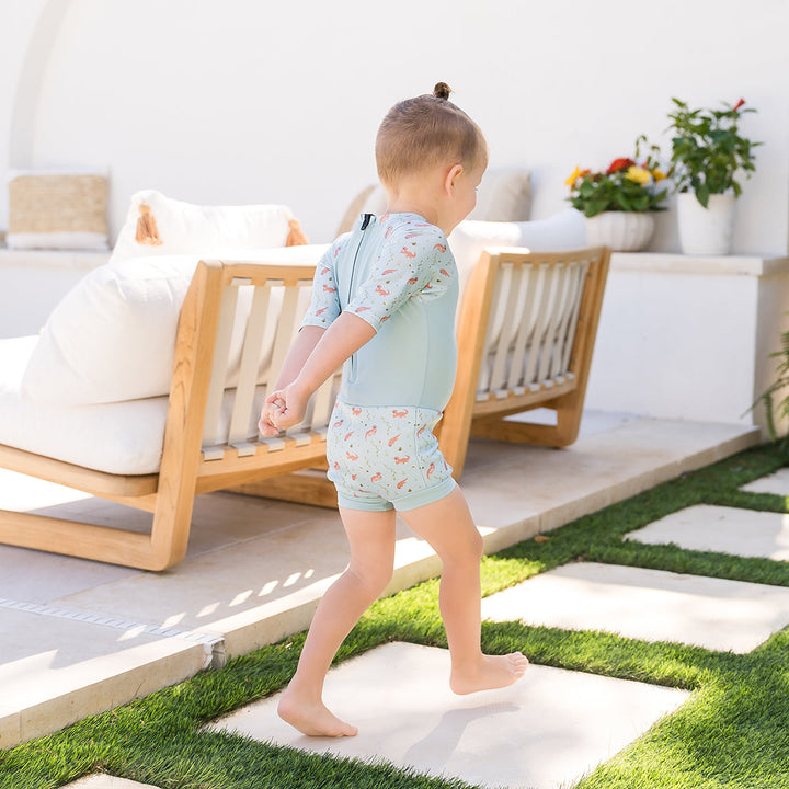Child wearing Happy Nappy Sunsuit in light blue and otters themed print. Back.