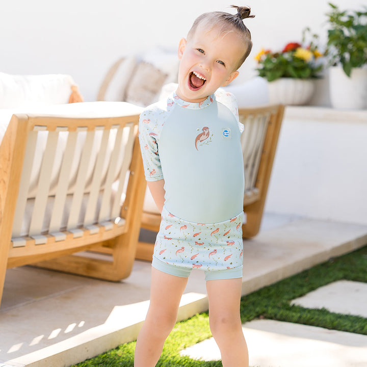 Child wearing Happy Nappy Sunsuit in light blue and otters themed print. Front.