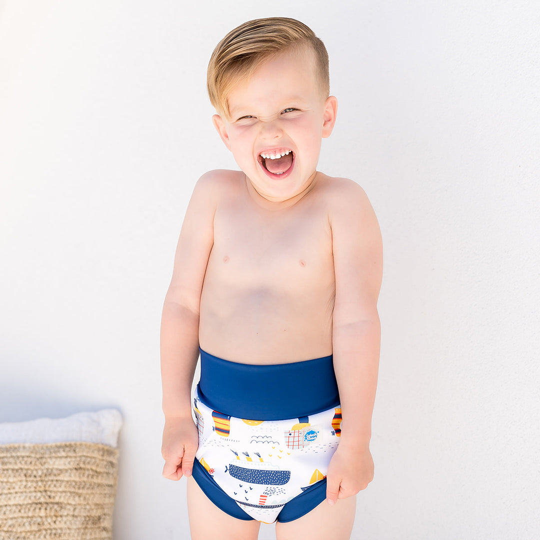 Little one wearing Happy Nappy in white with navy blue trims, featuring boats themed print. Front.