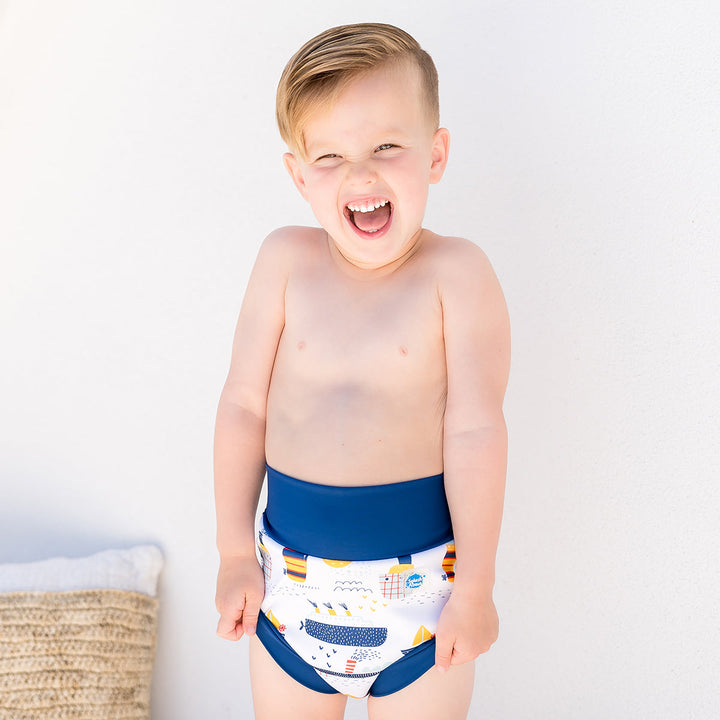 Little one wearing Happy Nappy in white with navy blue trims, featuring boats themed print. Front.