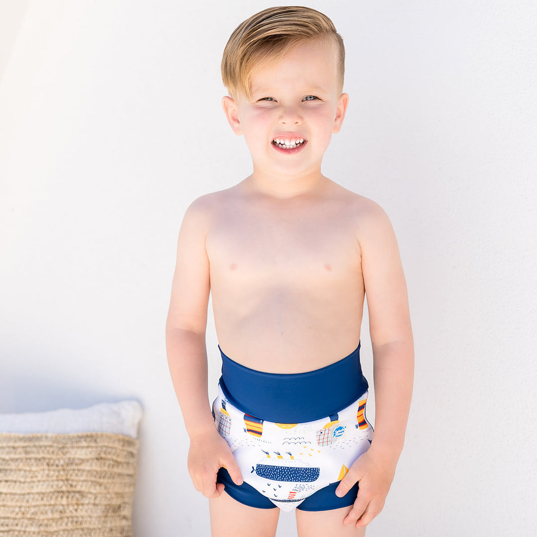Little one wearing Happy Nappy in white with navy blue trims, featuring boats themed print. Front.