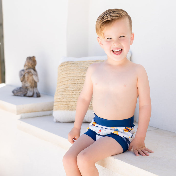 Little one wearing Happy Nappy in white with navy blue trims, featuring boats themed print. Side.