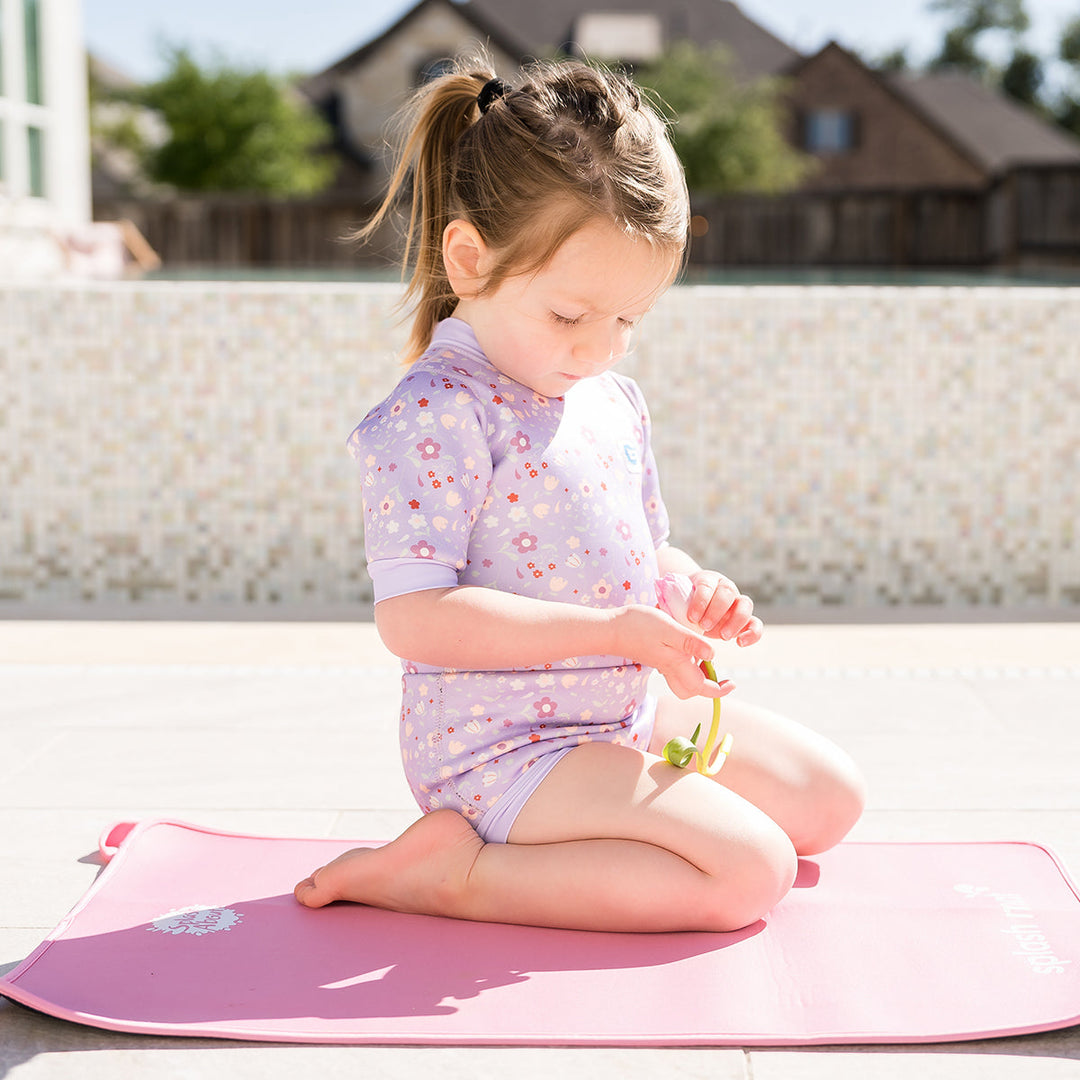 Child wearing baby wetsuit with built in swim nappy in lilac with floral themed print.