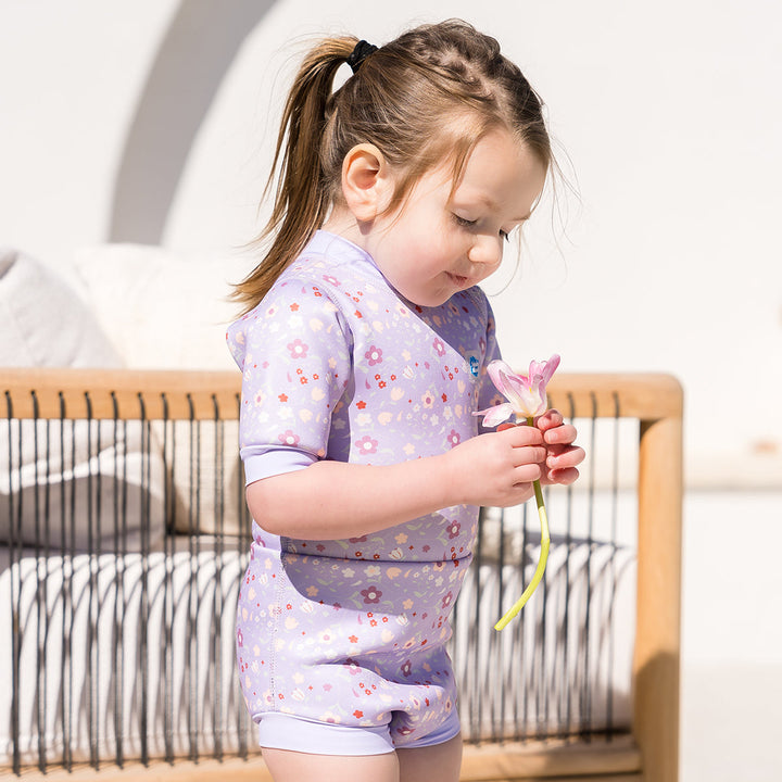 Child wearing baby wetsuit with built in swim nappy in lilac with floral themed print.
