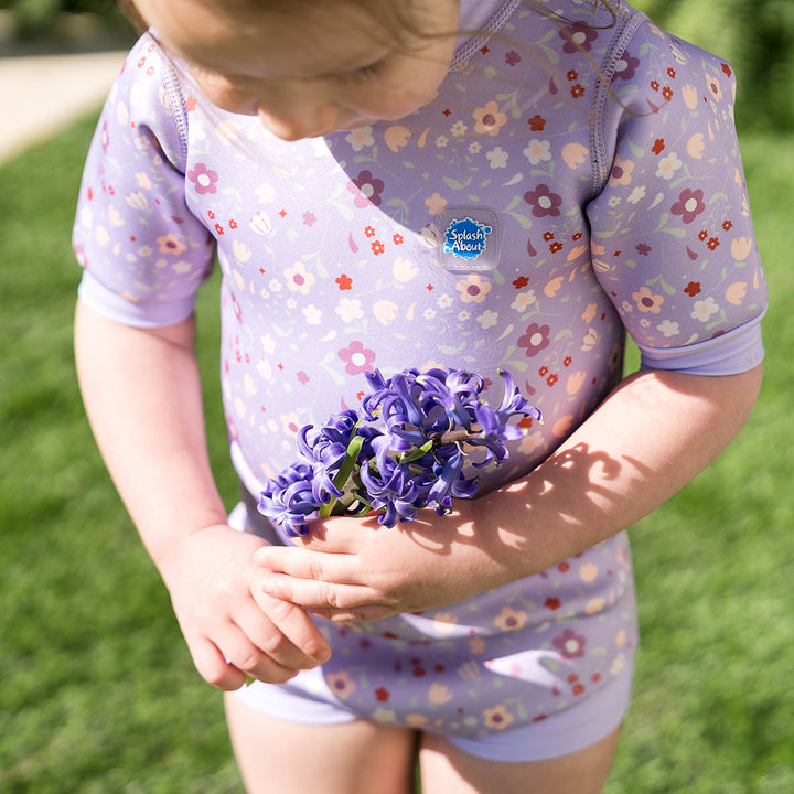 Child wearing baby wetsuit with built in swim nappy in lilac with floral themed print.
