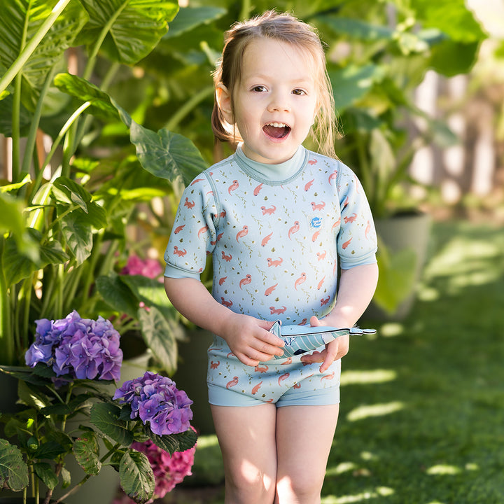 Child wearing baby wetsuit with built in swim nappy in light blue with otters themed print.