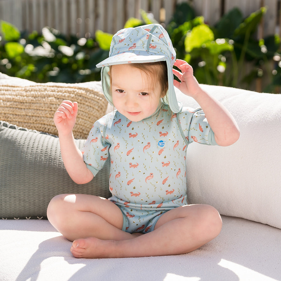 Child wearing baby wetsuit with built in swim nappy in light blue with otters themed print.