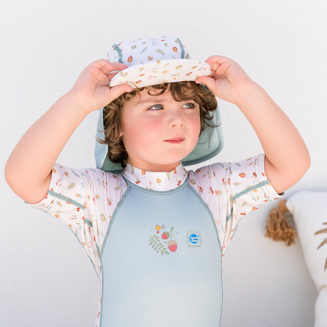 Little one wearing legionnaire style sun hat in light blue and white, with acorns and leaves themed print panel. They are also wearing matching wetsuit.