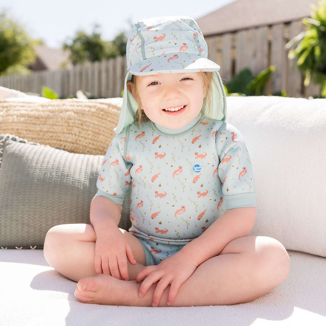 Little one wearing legionnaire style sun hat in light blue, with otters themed print panel. They are also wearing matching wetsuit.