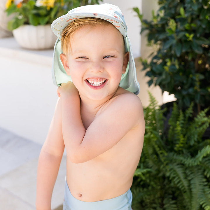 Little one wearing legionnaire style sun hat in light blue, with otters themed print panel.