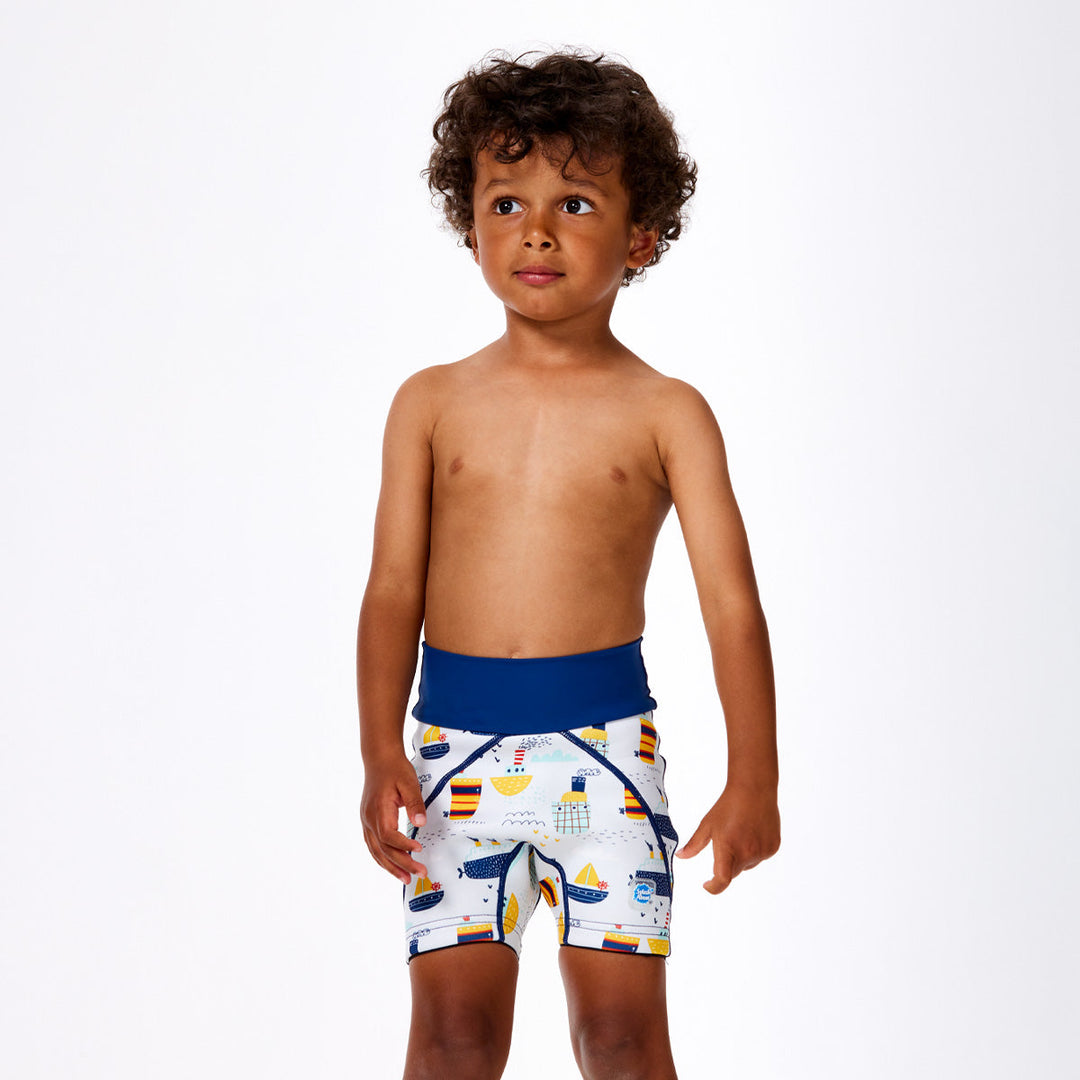 Little one wearing neoprene swim shorts in white with blue navy waist and boats themed print. Front.