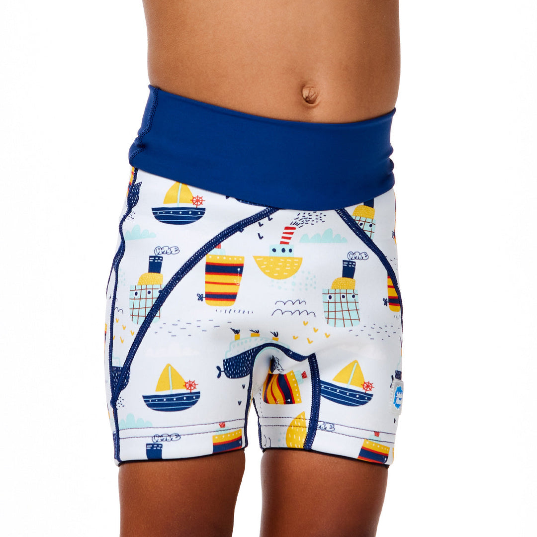Little one wearing neoprene swim shorts in white with blue navy waist and boats themed print. Close up.