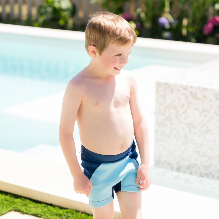 Child wearing neoprene swim shorts in blue and navy. Side.