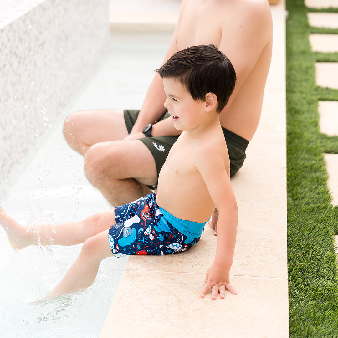 Child wearing neoprene swim shorts in navy, blue trims and under the sea themed print.