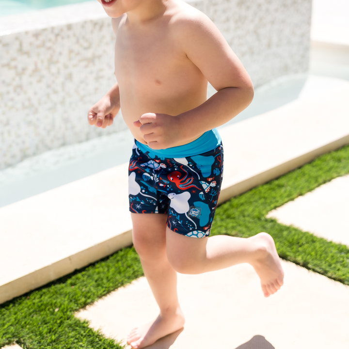 Child wearing neoprene swim shorts in navy, blue trims and under the sea themed print.