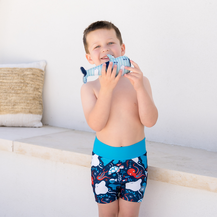 Child wearing neoprene swim shorts in navy, blue trims and under the sea themed print.