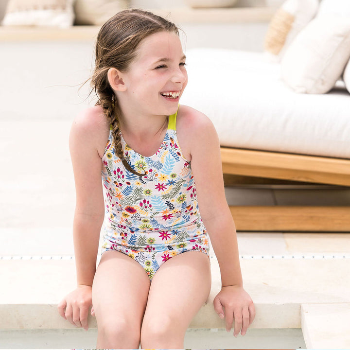 Girl wearing colourful jungle themed swimsuit with wide straps in bright lime poolside.