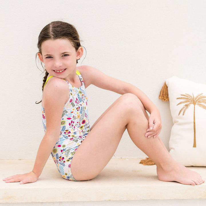 Girl wearing colourful jungle themed swimsuit with wide straps in bright lime poolside.