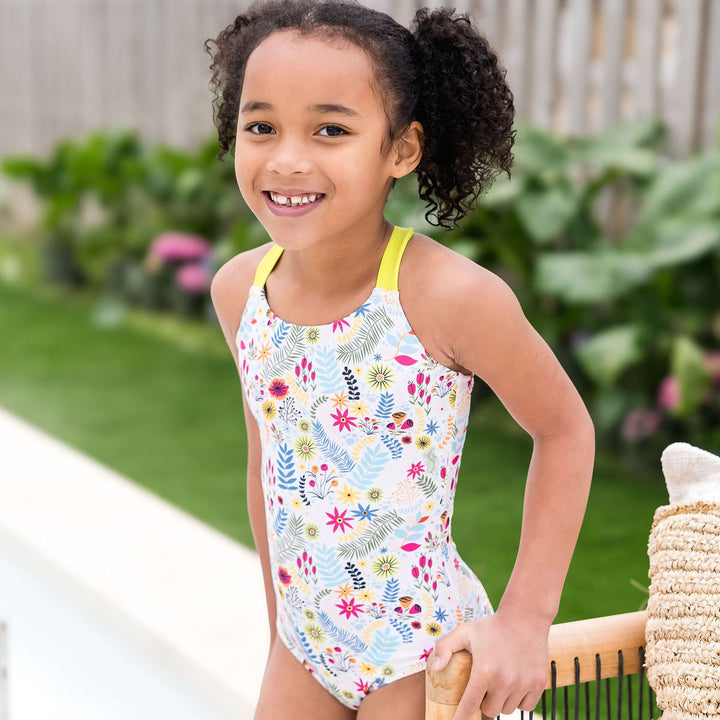 Girl wearing colourful jungle themed swimsuit over white background with wide straps in bright lime by the pool.