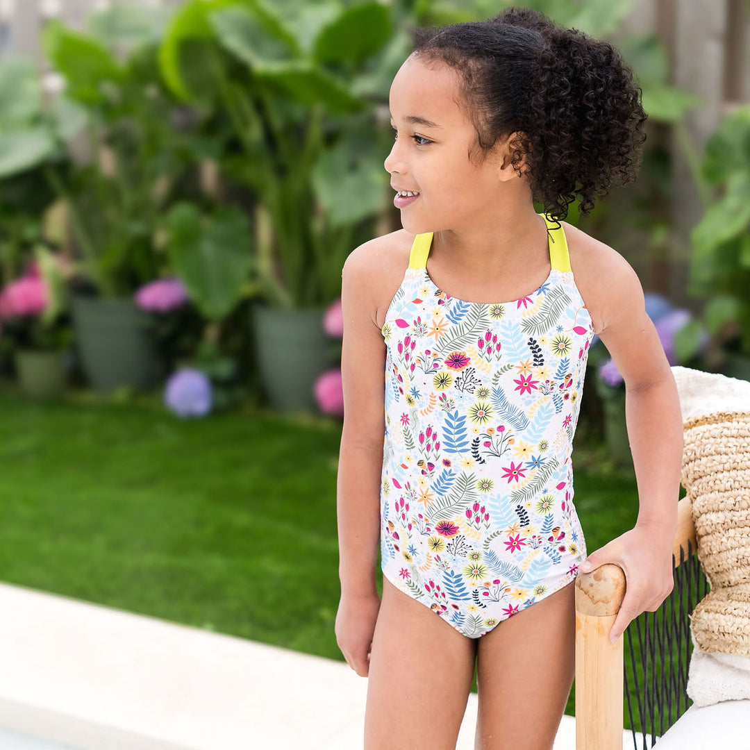 Girl wearing colourful jungle themed swimsuit over white background with wide straps in bright lime by the pool.