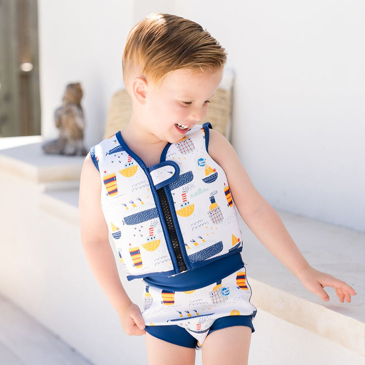 Lifestyle image of child wearing neoprene swim vest for toddlers with non-removable floats in white, navy trims and boats themed print. He's also wearing matching Happy Nappy. Front.