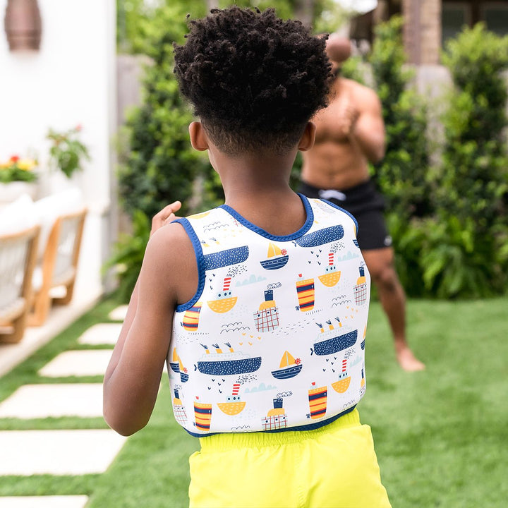 Lifestyle image of child wearing neoprene swim vest for toddlers with non-removable floats in white, navy trims and boats themed print. Back.