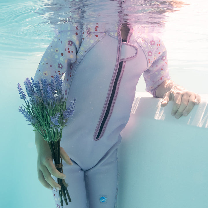 Kid swimming in shorty wetsuit in lilac, featuring floral themed print in sleeves and side panels.