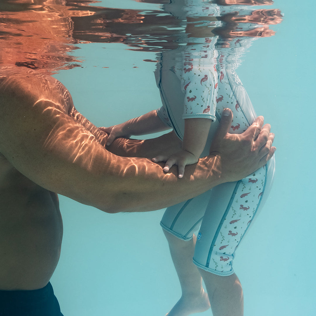 Kid swimming in shorty wetsuit in light blue, featuring otters themed print in sleeves and side panels.