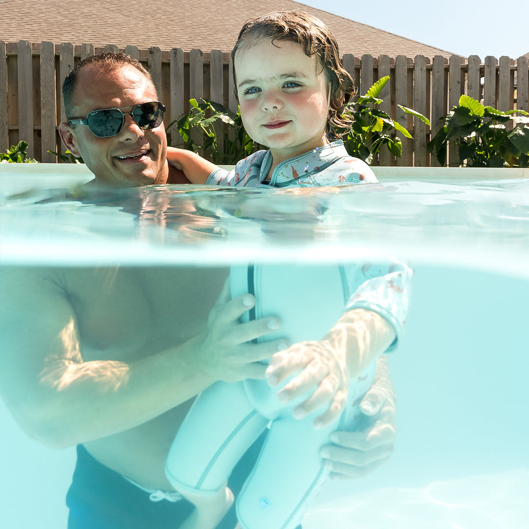 Kid swimming in shorty wetsuit in light blue, featuring otters themed print in sleeves and side panels.