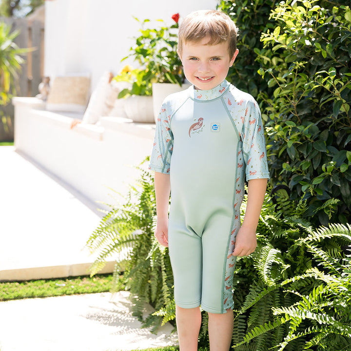 Child wearing one piece UV sun and sea wetsuit for toddlers in light blue, featuring otters themed print on sleeves, side panels, neck and chest.