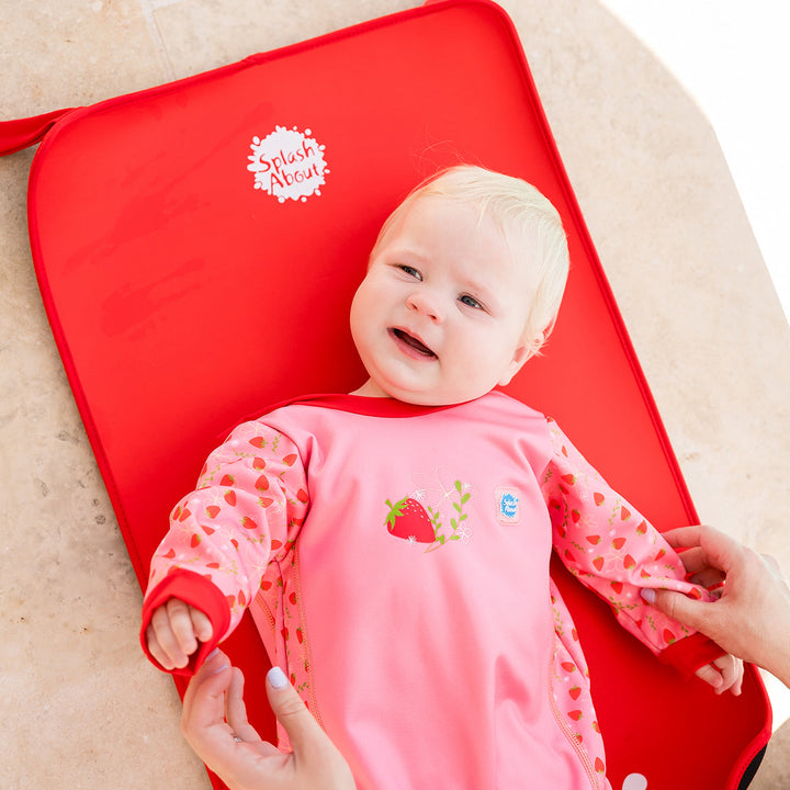 Child wearing strawberry themed baby wetsuit in pink with red trims.