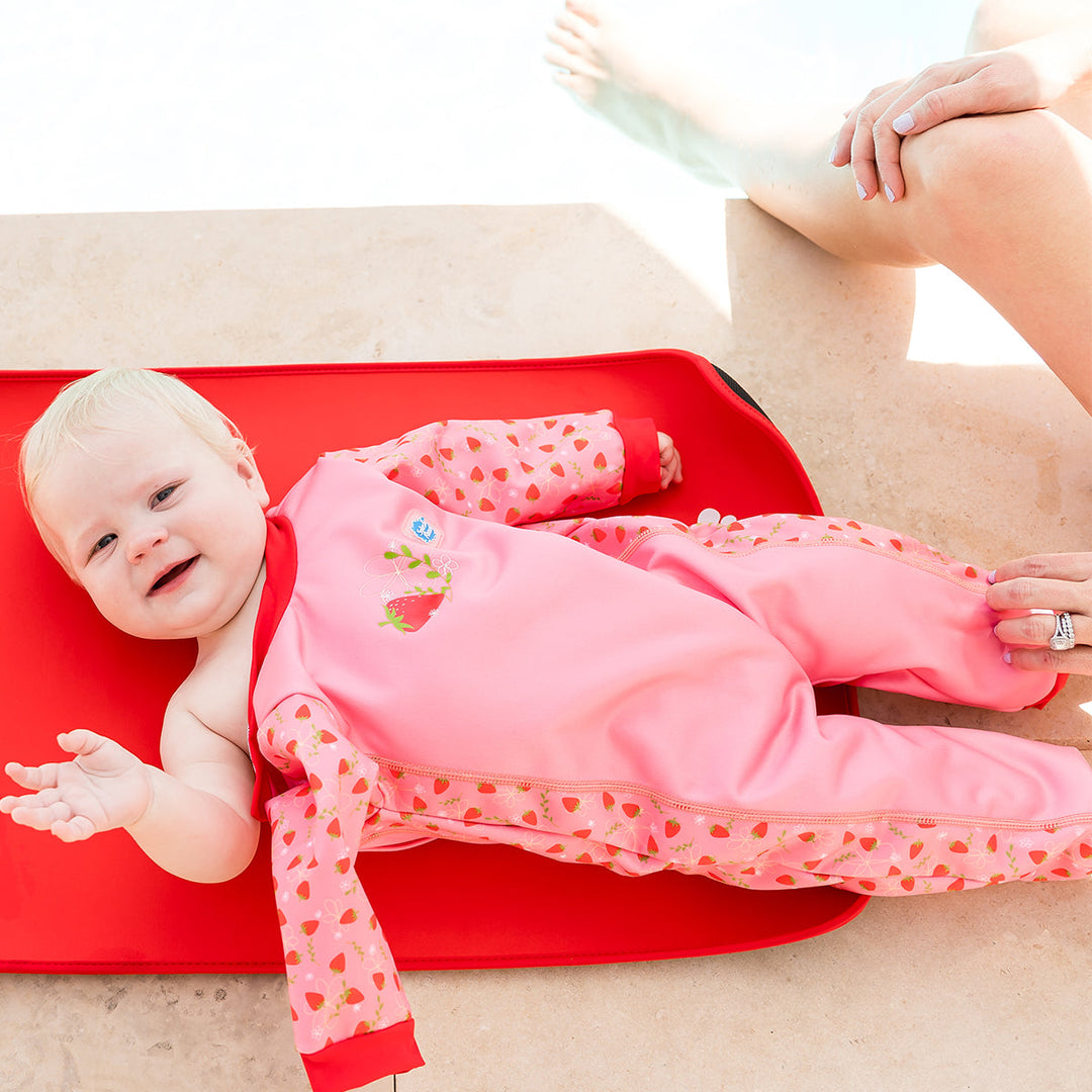 Child wearing strawberry themed baby wetsuit in pink with red trims.