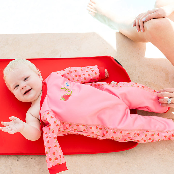 Child wearing strawberry themed baby wetsuit in pink with red trims.