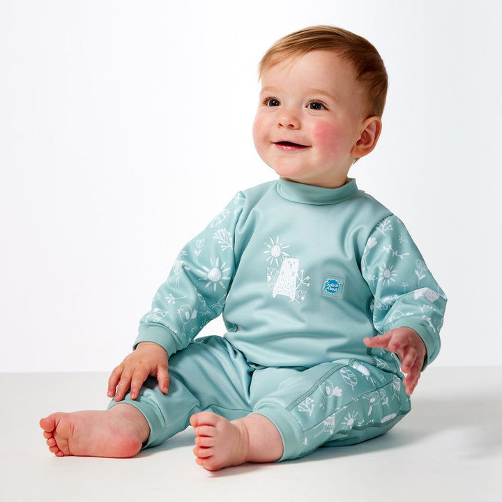 Little one wearing fleece-lined baby wetsuit in greenish blue and white with animals themed print, including bears, llamas, suns and flowers on arms, side panels and chest. Side.